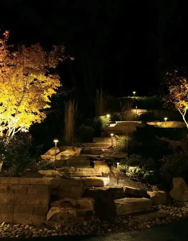 Lit stone steps through a landscaped garden at night, lit by warm path lights and framed by autumn trees.
