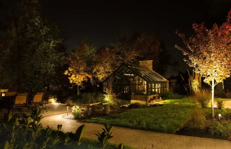 Lit garden path at night with glowing trees and a house in the background