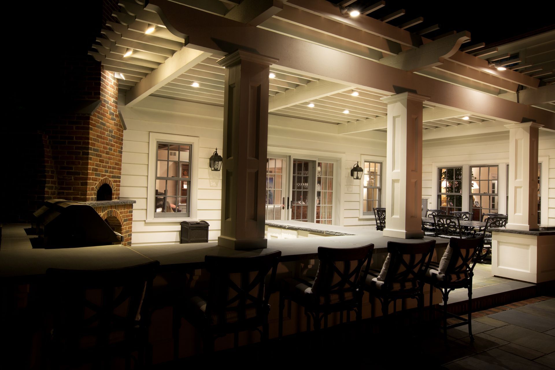 Landscaper kneels by a lit garden path, adjusting a spotlight beside shrubs and tools at night.