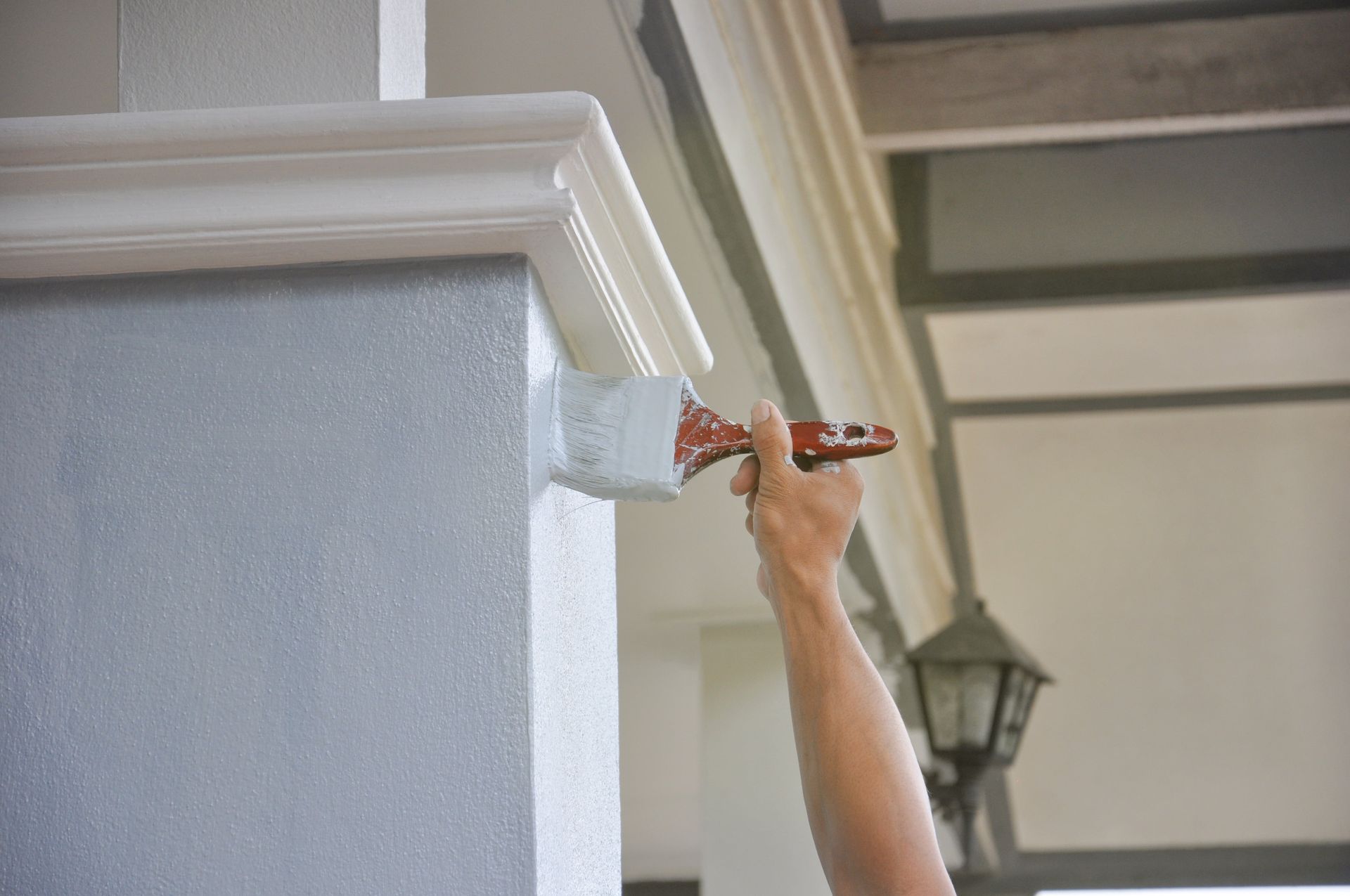 Hand painting the exterior trim of a house with a brush and white paint