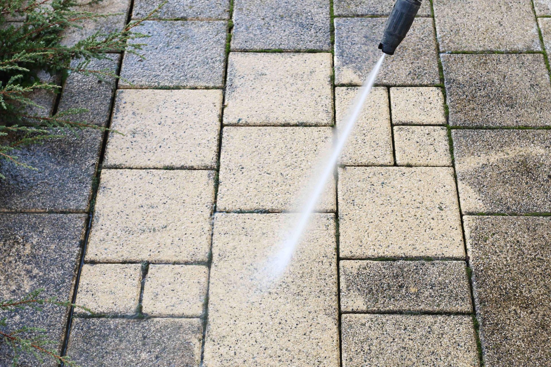Pressure washing beige and gray patio pavers with a spray wand
