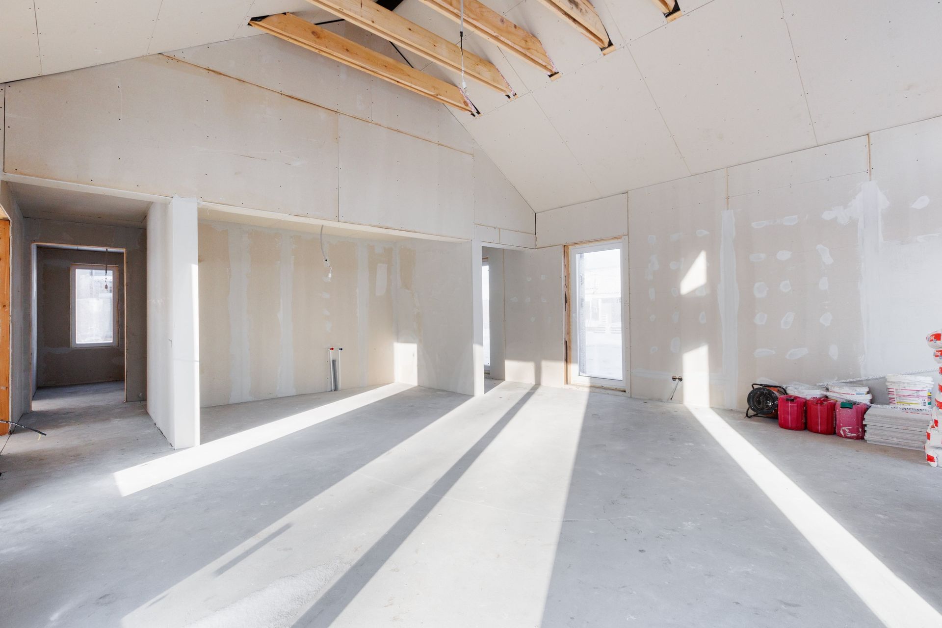 Empty unfinished room with drywall, exposed rafters, and bright sunlight on the floor