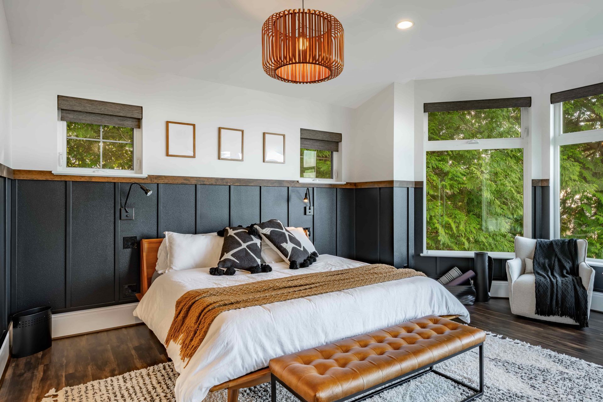 Modern bedroom with a wooden bed, dark wainscoting, and large windows overlooking greenery