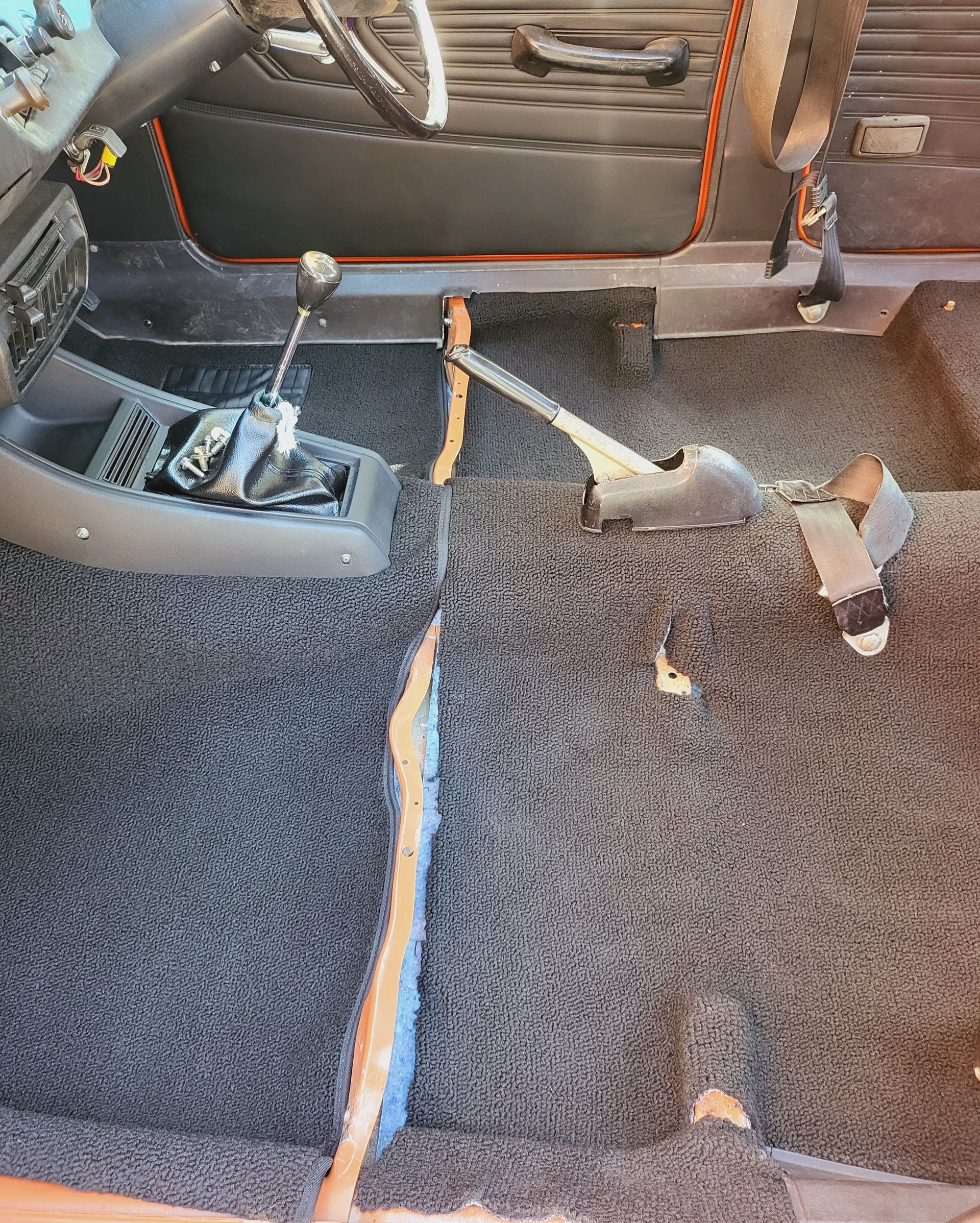Car interior with dark gray carpet, gear shift, and parking brake visible.