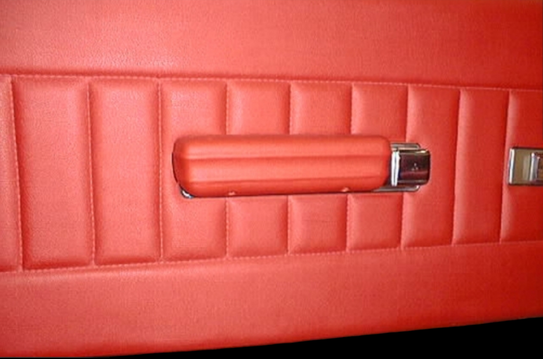 Red car door panel with padded rectangular sections and a red armrest with chrome accents.