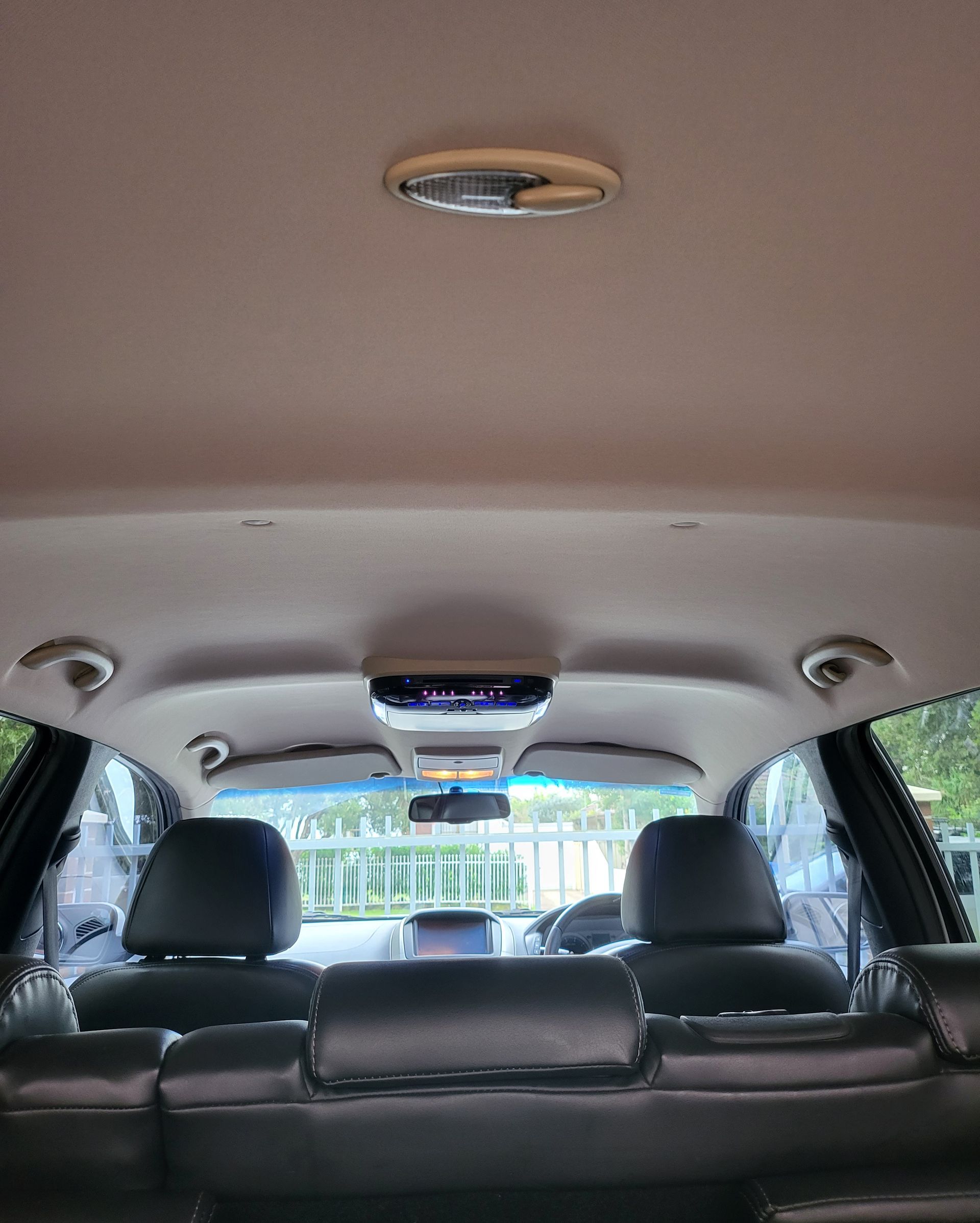 Interior of a car; black seats, light-colored ceiling with overhead console, view through front seats.