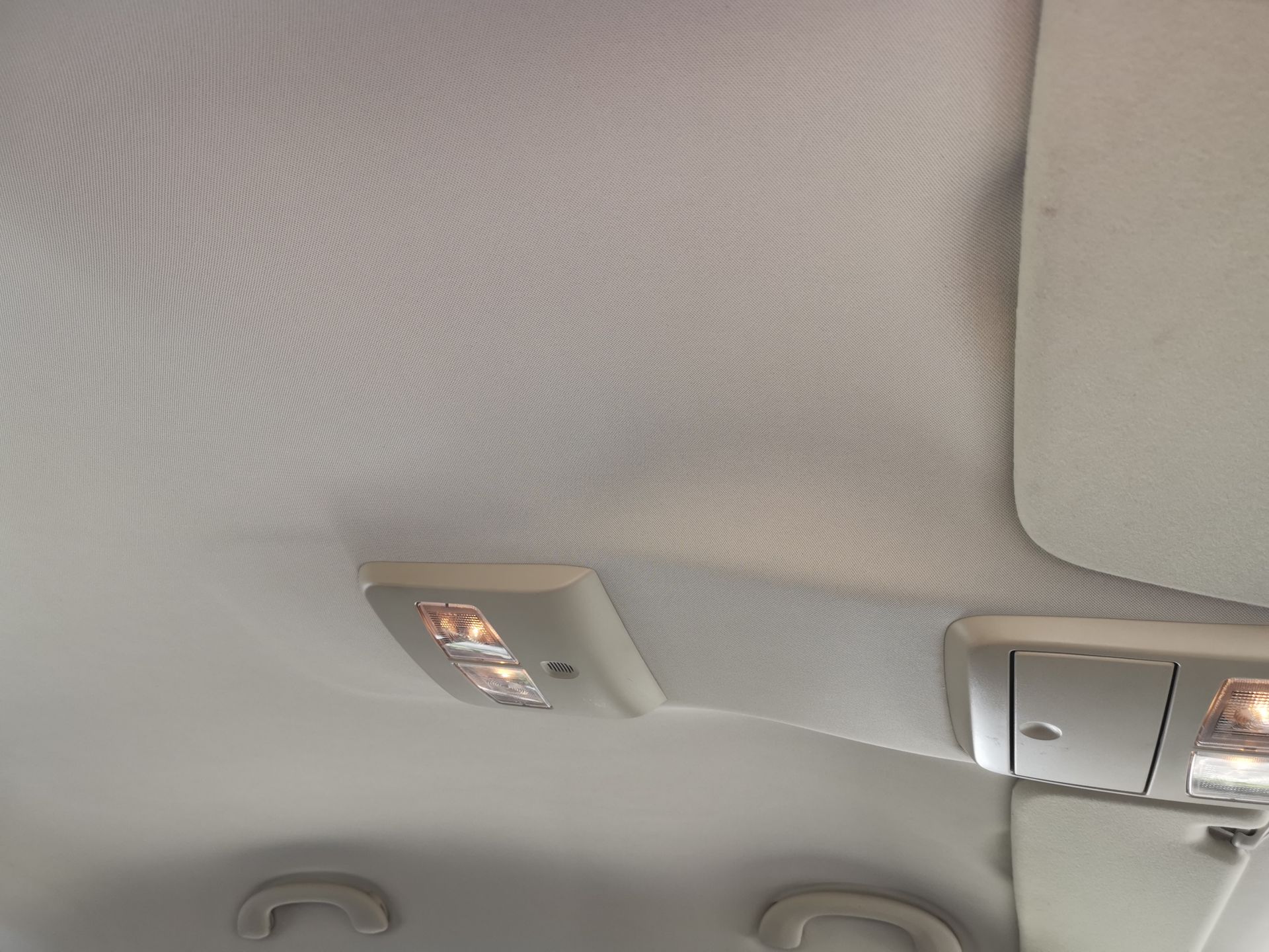 Car's white interior ceiling with two overhead lights and sun visor.