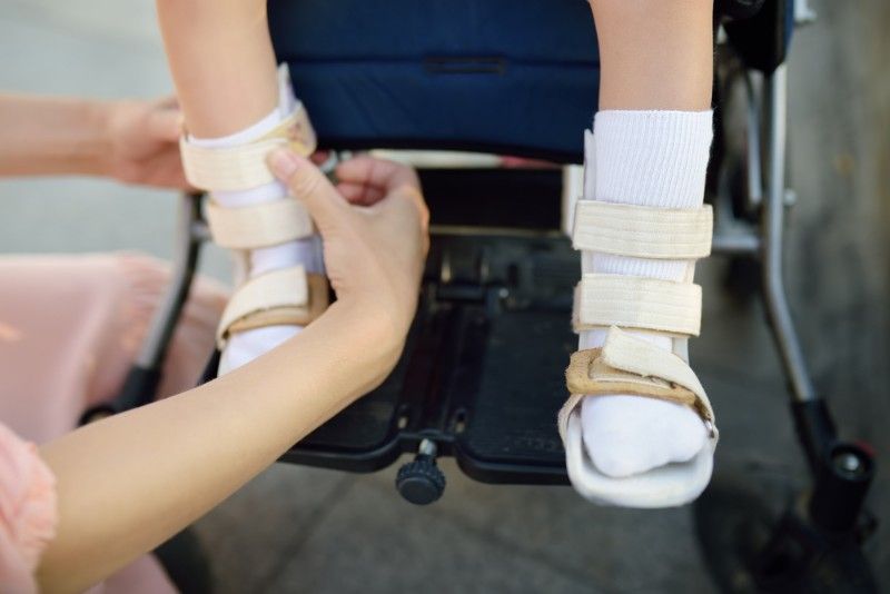 Person Adjusting Leg Braces on a Child in a Wheelchair, Outdoors — Ballina Home Healthcare Sales & Hire and Compression Stockings Plus in Ballina, NSW