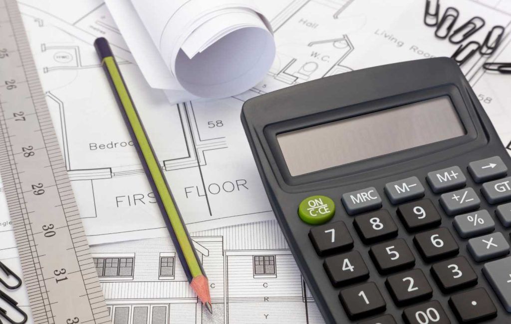 Architectural blueprints, calculator, pencil, and ruler on a desk.