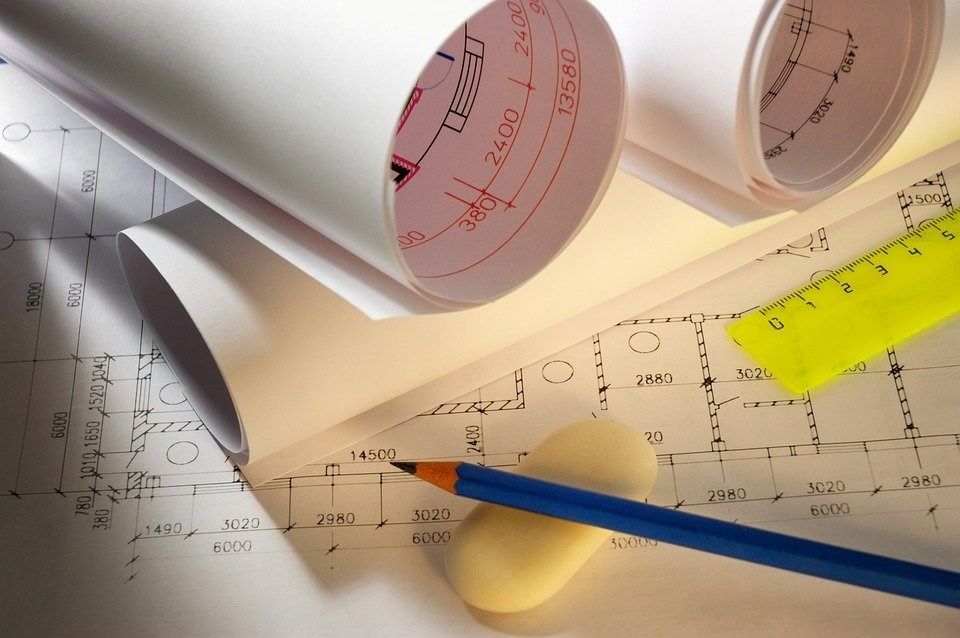 Architectural blueprints, pencil, eraser, and ruler on a table.