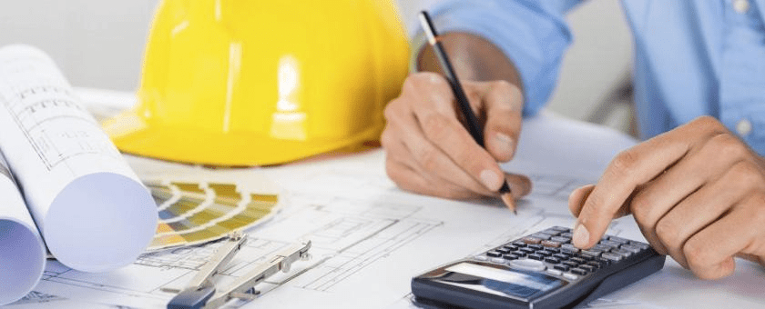 Person working on blueprints with a calculator, pen, yellow hard hat, and color swatches.
