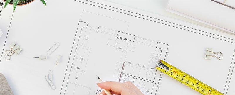 Hand drawing on a blueprint, with a measuring tape.