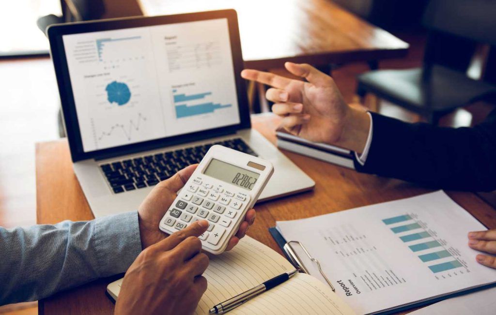 Two people analyzing financial data on a laptop, calculator, and papers.