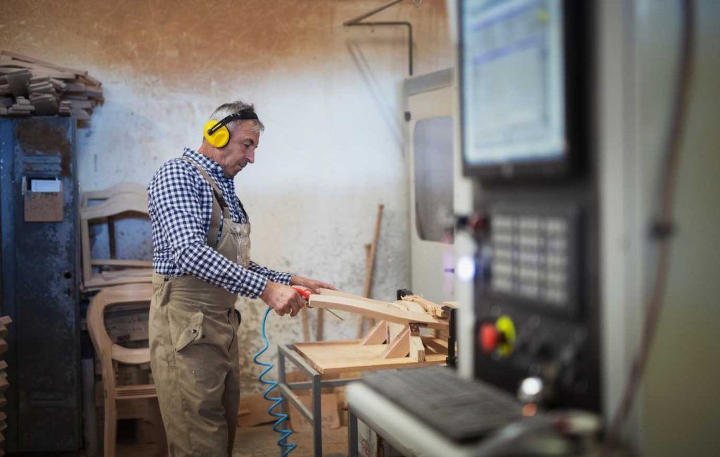 Man in a woodworking shop using a CNC machine, wearing hearing protection.