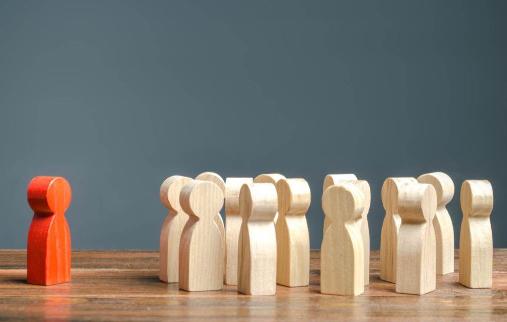 Red figure facing away from group of light wooden figures, implying leadership or difference.