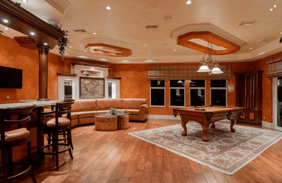 Orange-toned luxury game room with bar, pool table on rug, and seating.