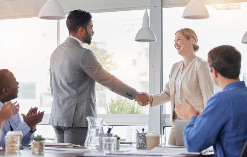 Man and woman shaking hands in a business meeting. Colleagues clap, bright setting.