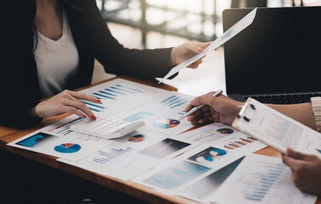 Two business people reviewing charts and data on a desk, using calculator and pen.