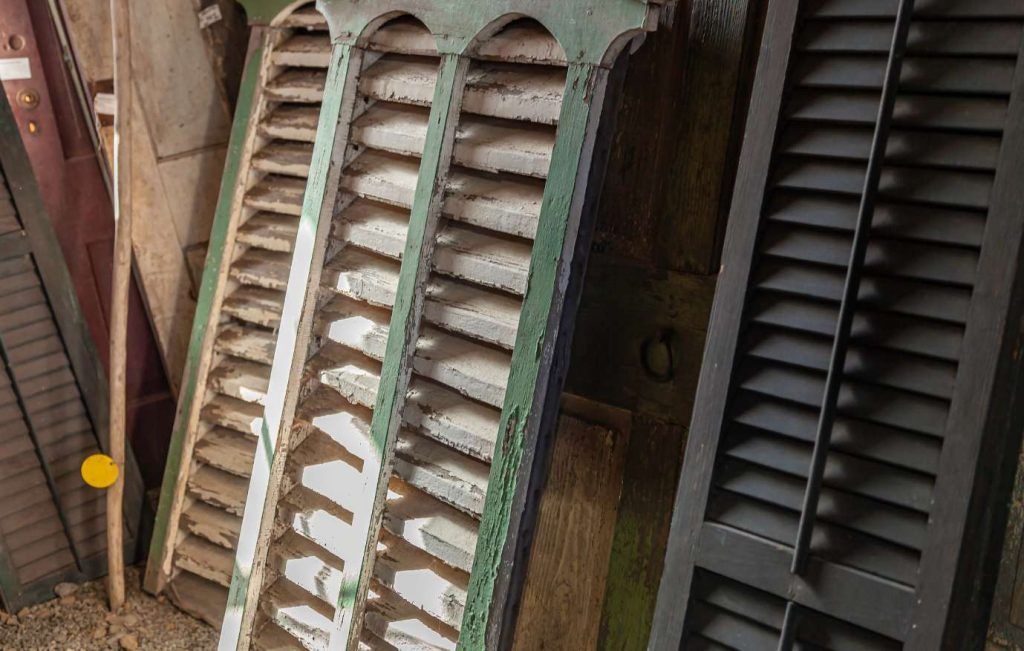 Old wooden shutters of varying colors and styles, leaning against a wall.