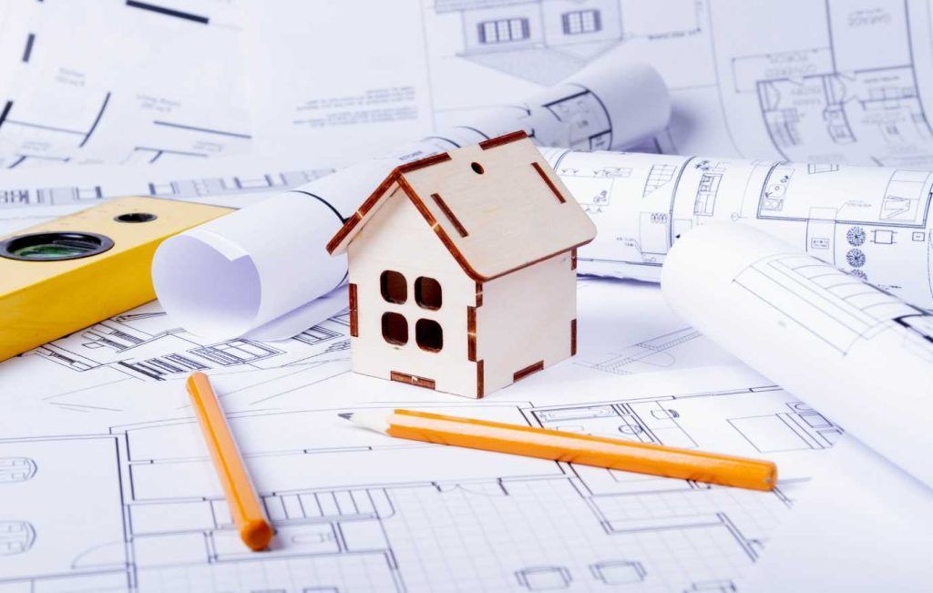 Miniature house on architectural blueprints, with pencils and level, representing construction plans.