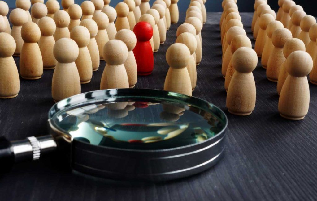 Magnifying glass over wooden figures, one red, symbolizing focus and analysis.