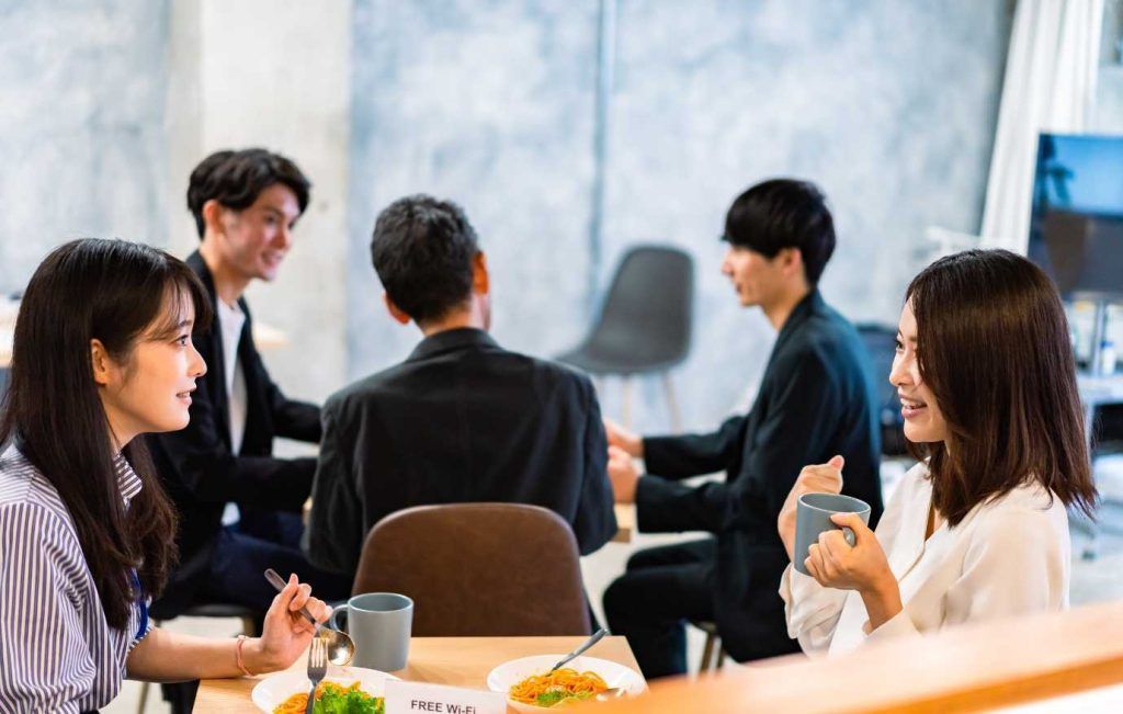 Five businesspeople in a cafe, smiling and talking around a table.