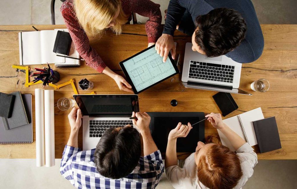 Team of diverse colleagues collaborating around a wooden table, using laptops and tablets, brainstorming.