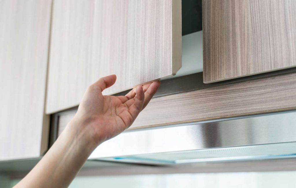 Hand reaching for a light wood kitchen cabinet door.