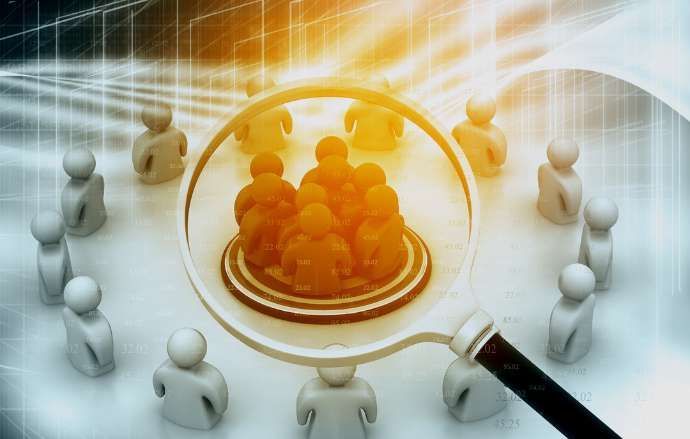 Magnifying glass focusing on a group of people in a target; other people surround.