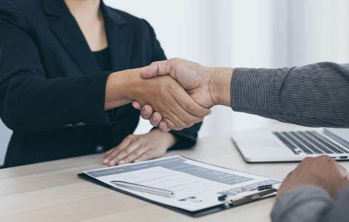 Two people shaking hands over a document on a desk; business deal.