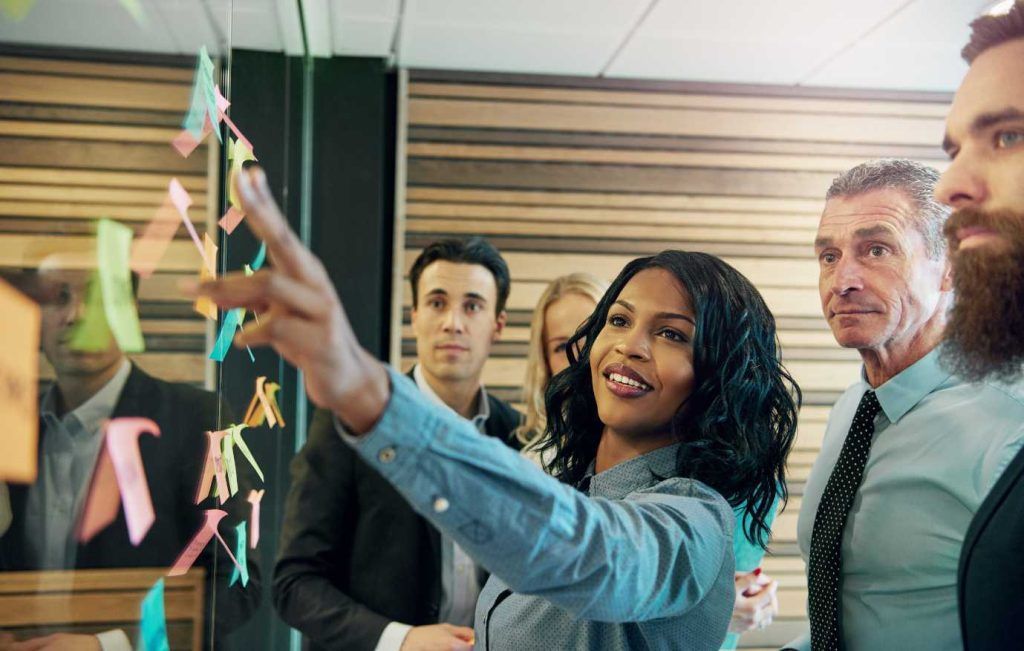 Group of business people brainstorming using sticky notes on a glass wall.