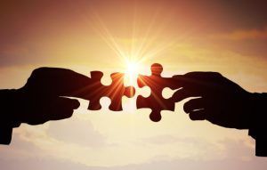 Silhouette hands connecting puzzle pieces against a sunset.