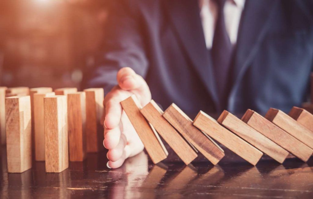A person in a suit stopping a row of wooden blocks from toppling over, symbolizing risk management.