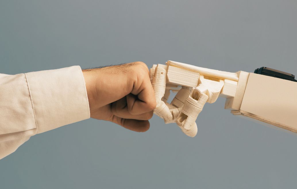Human fist bumps a white robotic hand against a blue background.