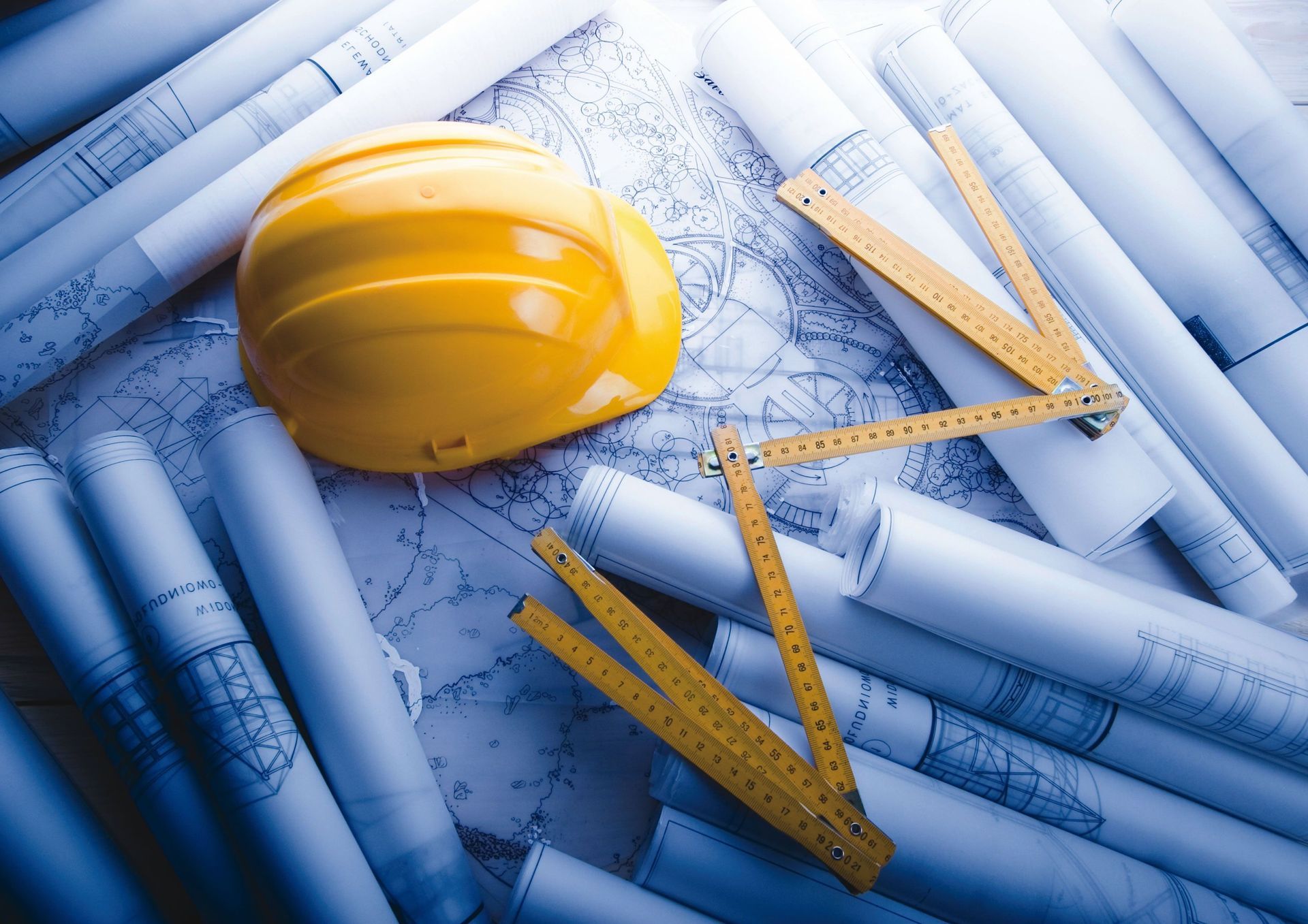 Yellow hard hat and folding ruler atop architectural blueprints.