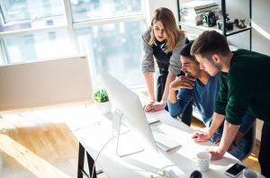 Three people looking at a computer screen, brainstorming in a bright office.