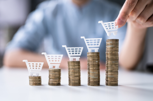 Person stacking coins with toy shopping carts, representing growing consumer spending.