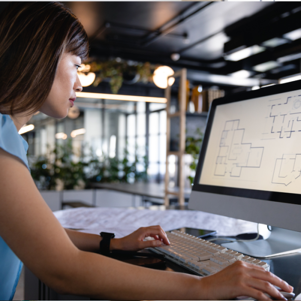 Woman working on a computer, looking at architectural plans in a modern office.