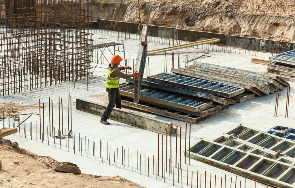 Construction worker in orange hard hat and vest, placing forms amid steel reinforcement.