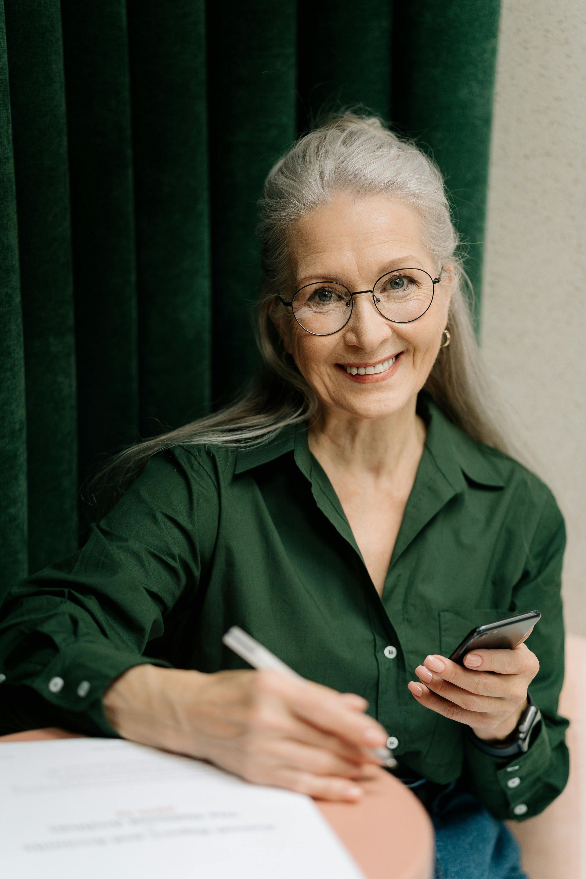 An elderly woman is wearing glasses and smiling.