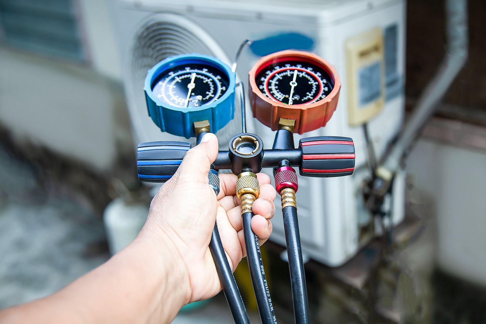 A person holding gauges to test an air conditioning unit with red and blue dials.