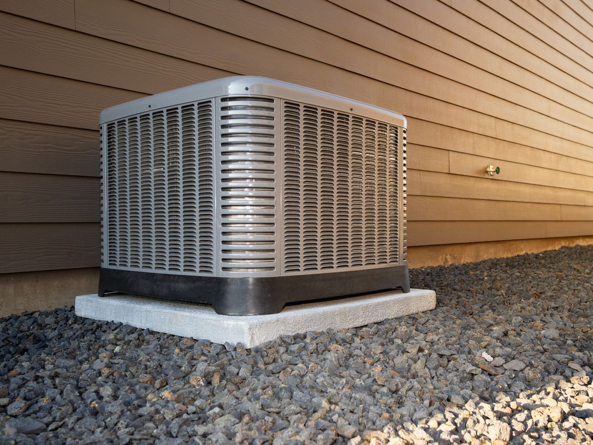 An air conditioner is sitting on top of a pile of gravel next to a house.