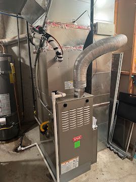 A furnace is sitting in a basement next to a water heater.