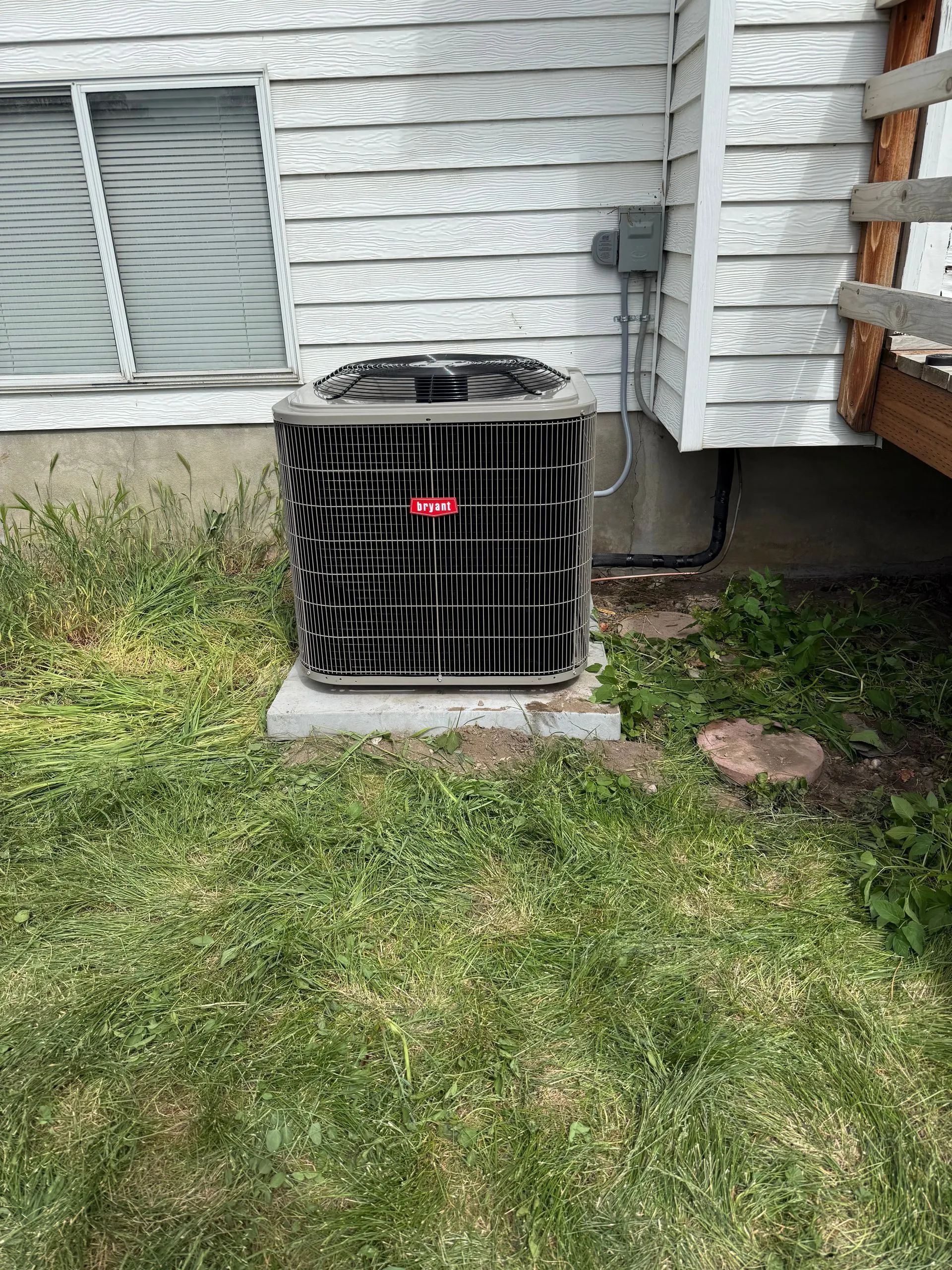 Air conditioning unit outside a building, on a concrete base, with green grass around it.