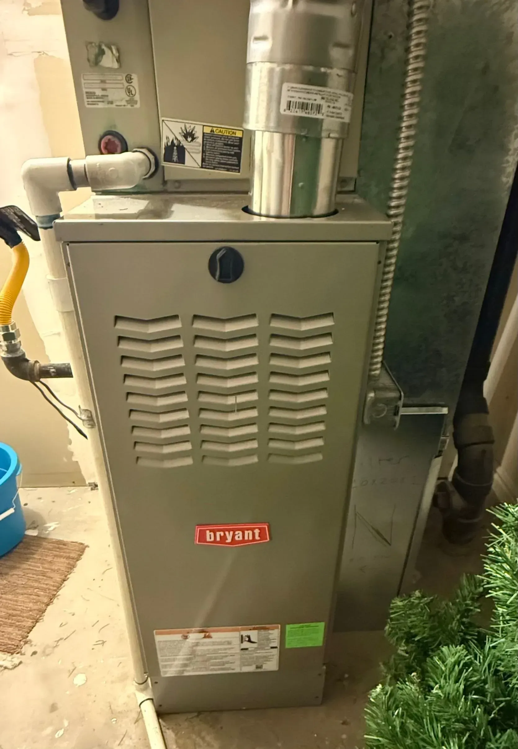 Gray gas furnace in a utility closet beside ductwork and pipes.
