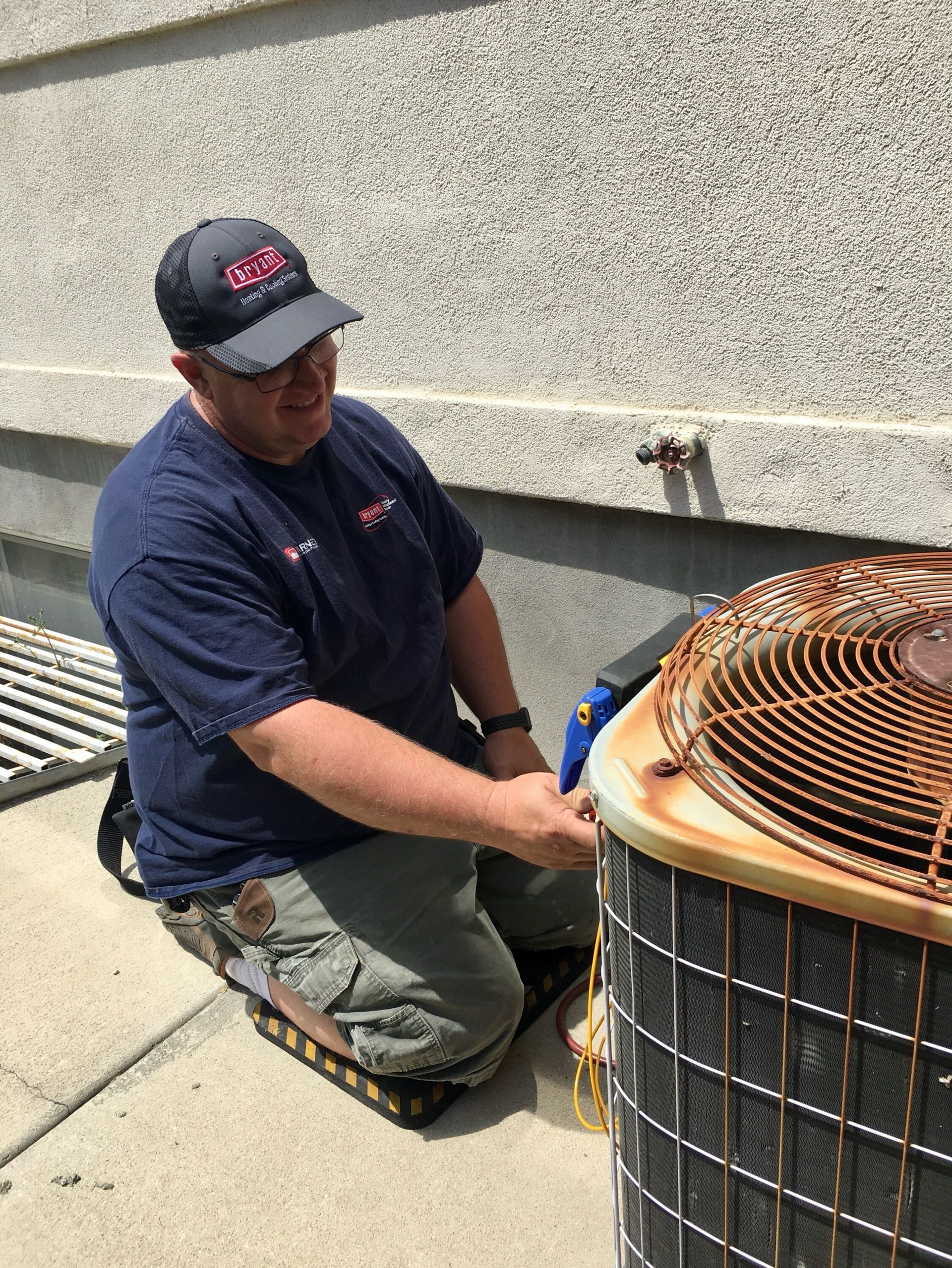 A man is kneeling down next to an air conditioner.