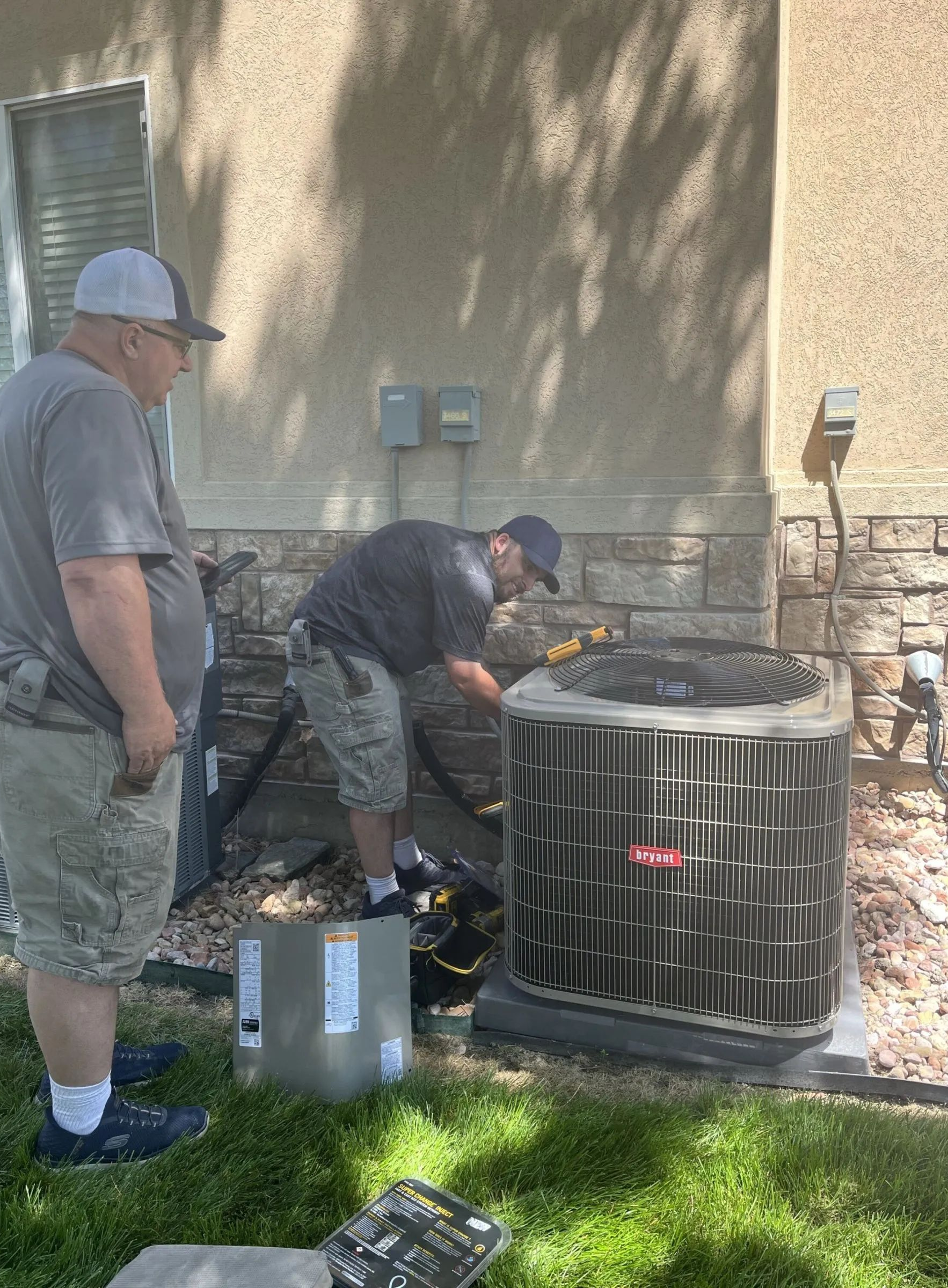 Two people in work attire performing maintenance on an outdoor residential air conditioning unit.