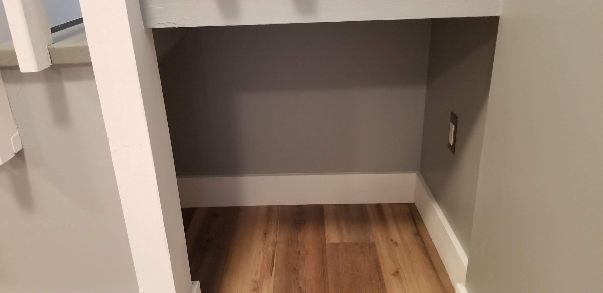 There is a small closet under the stairs with a wooden floor.