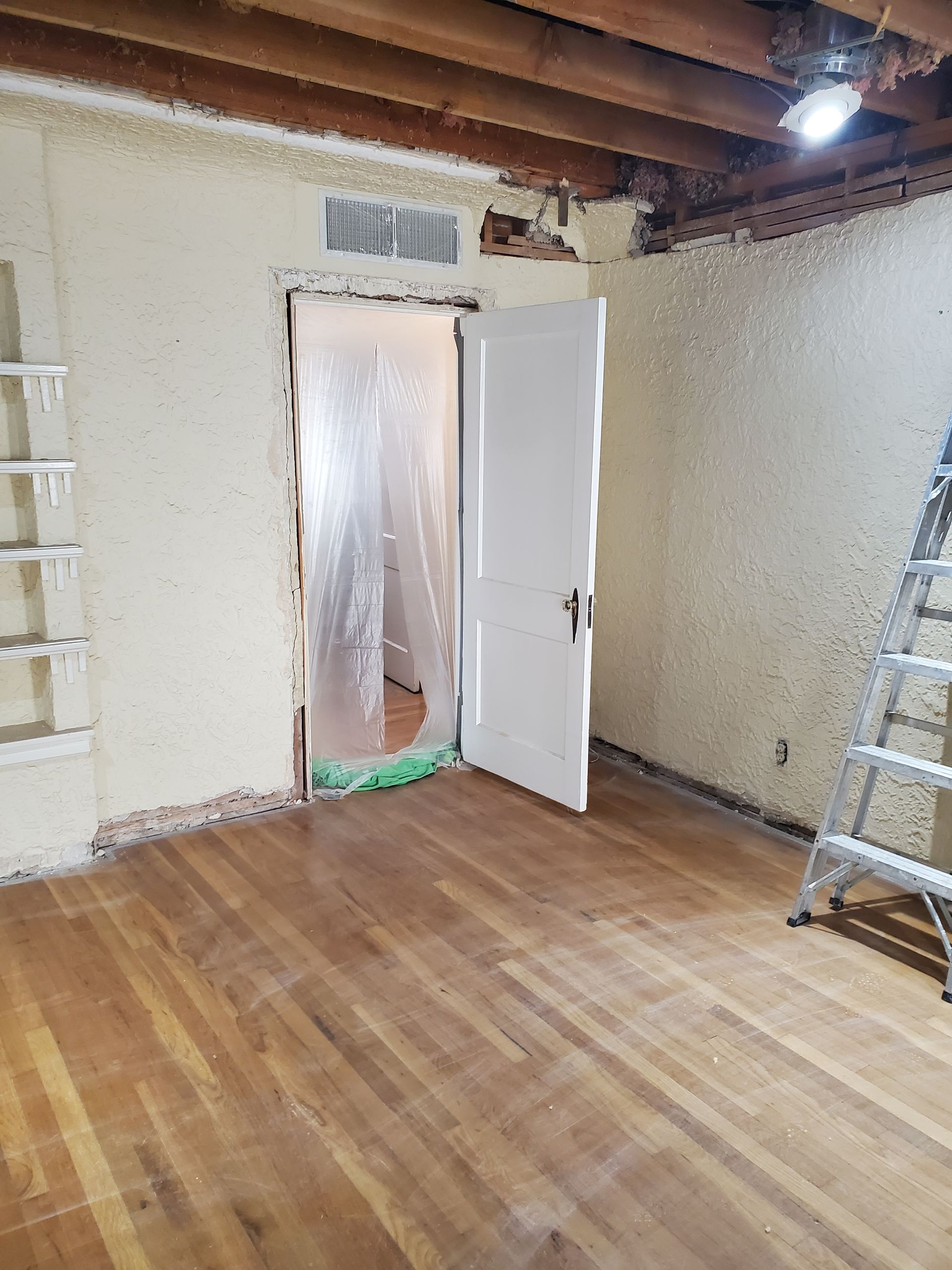 An empty room with hardwood floors and a ladder.