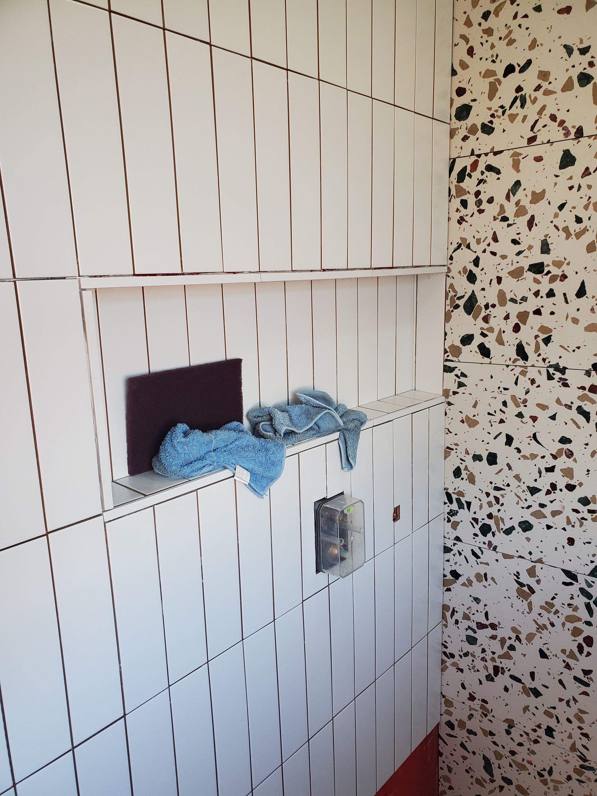 A white tiled wall with a blue cloth on a shelf